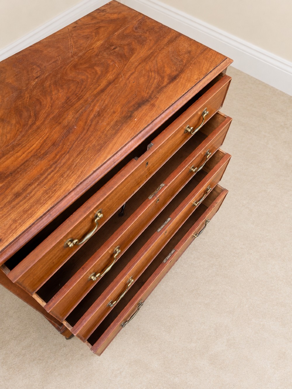 An antique Georgian mahogany chest of drawers featuring four graduated drawers with brass swan-neck handles, keyhole escutcheons, and bracket feet. View VI