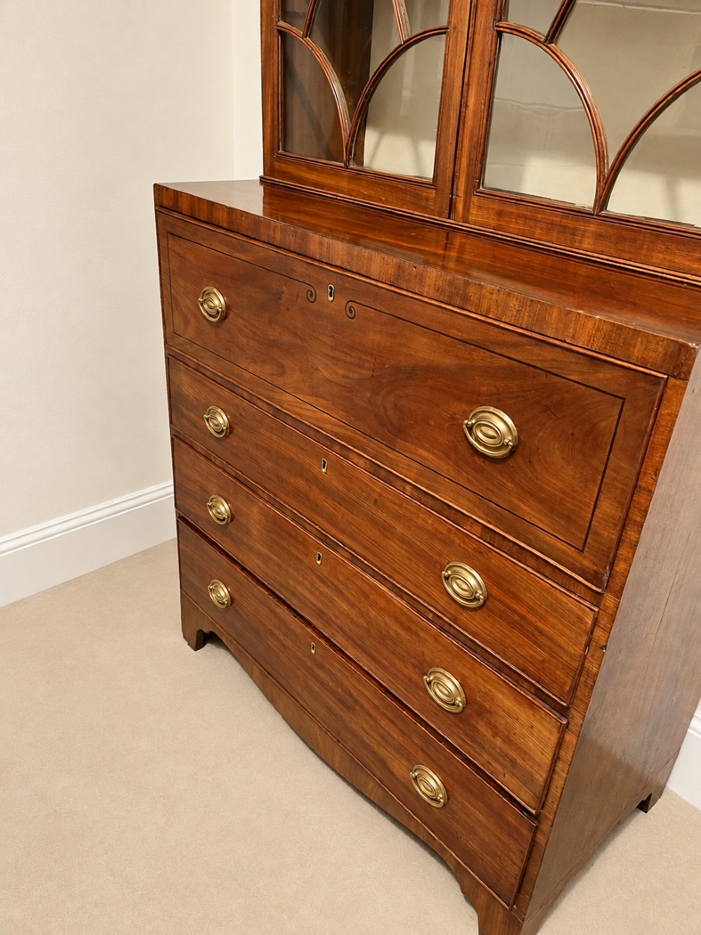 A 19th-century mahogany secretaire bookcase featuring an arched pediment, astragal glazed upper doors, and a four-drawer base with circular brass handles. View V