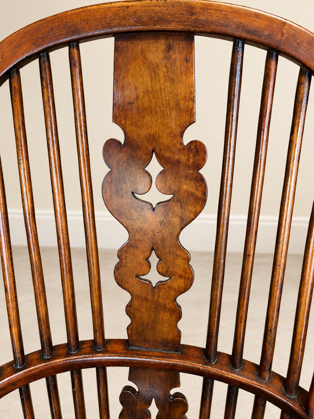 An antique 19th-century wooden Windsor armchair featuring a hoop back with turned spindles, a central pierced splat, a contoured saddle seat, and curved armrests supported by turned front legs. View V