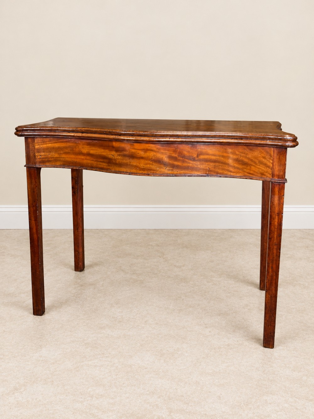 An antique Georgian dark mahogany fold-over table featuring a serpentine-curved front apron and four straight legs. View III