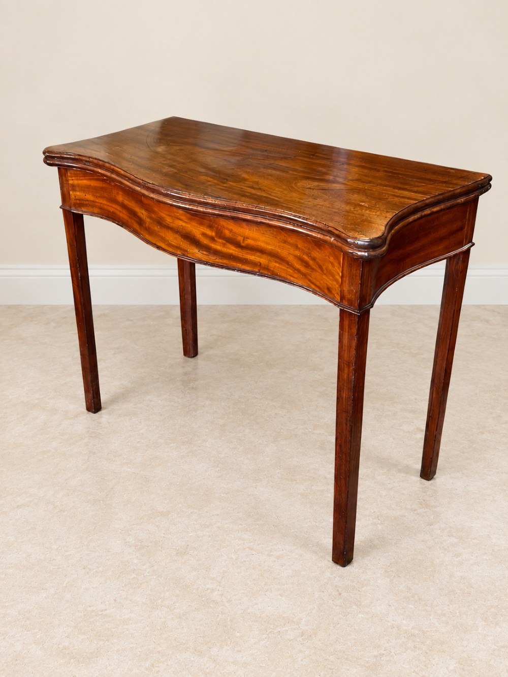 An antique Georgian dark mahogany fold-over table featuring a serpentine-curved front apron and four straight legs. View IV
