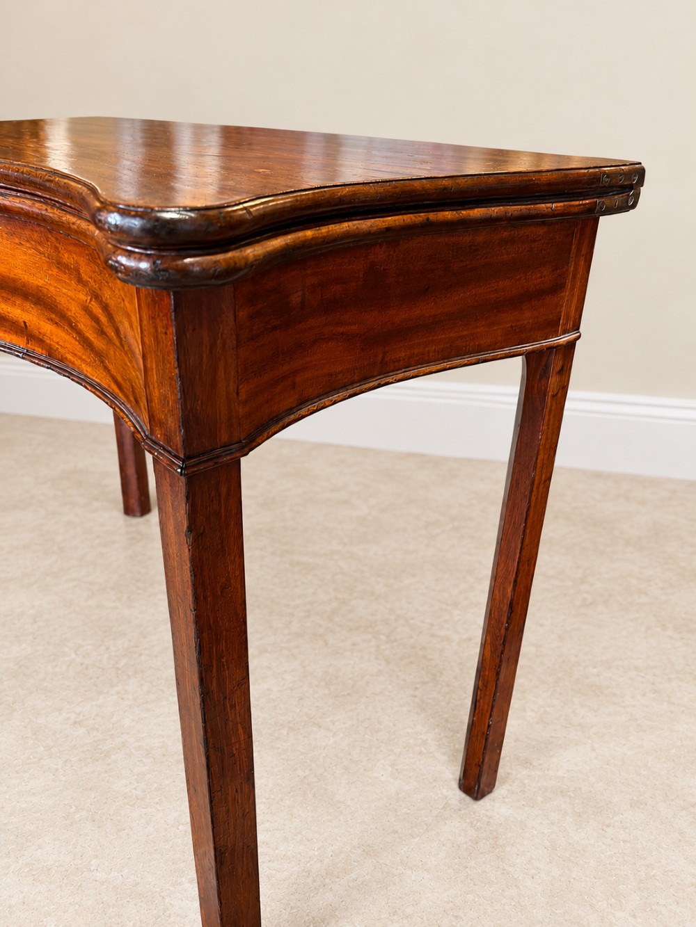 An antique Georgian dark mahogany fold-over table featuring a serpentine-curved front apron and four straight legs. View VI