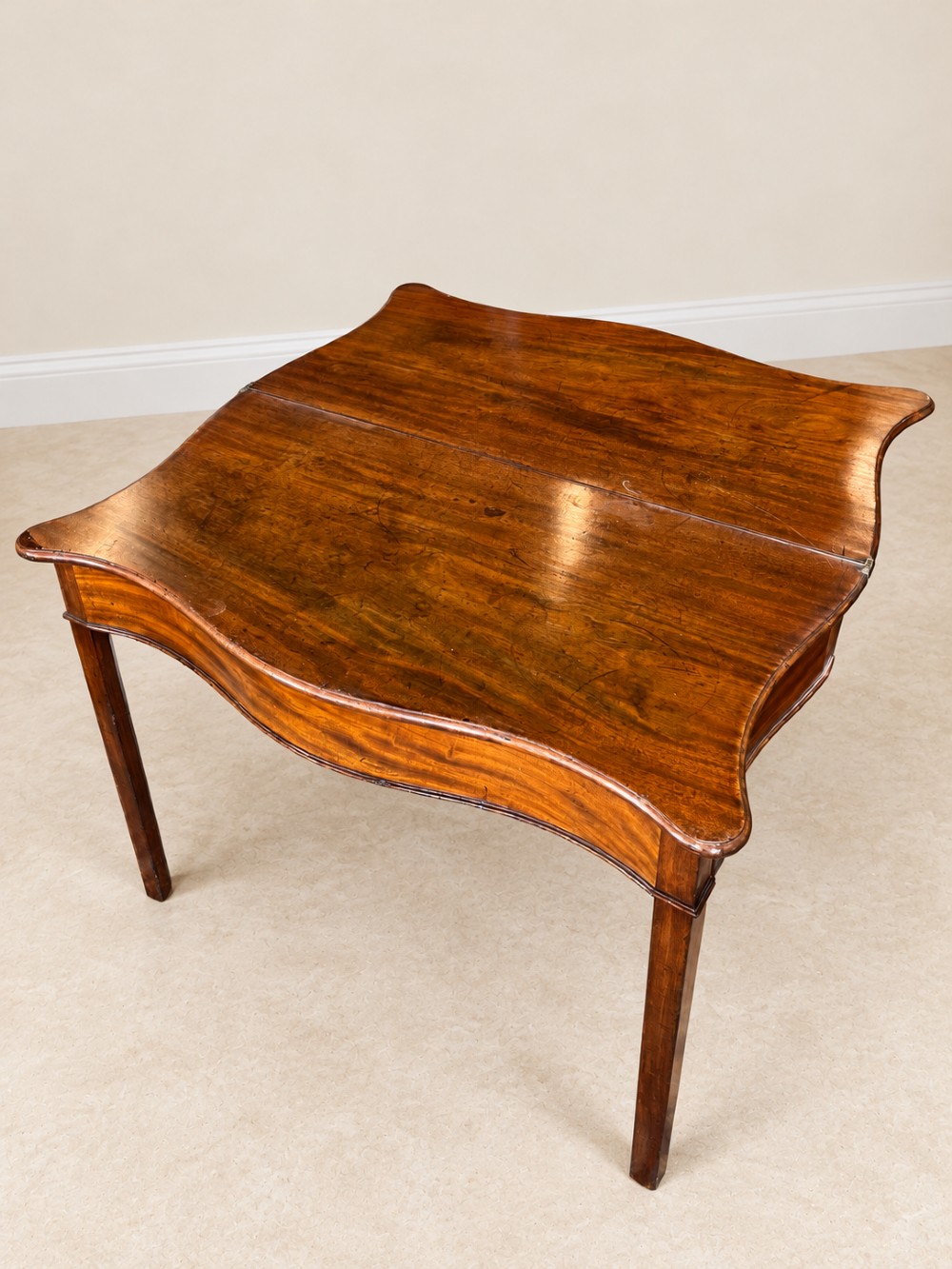 An antique Georgian dark mahogany fold-over table featuring a serpentine-curved front apron and four straight legs. View IX