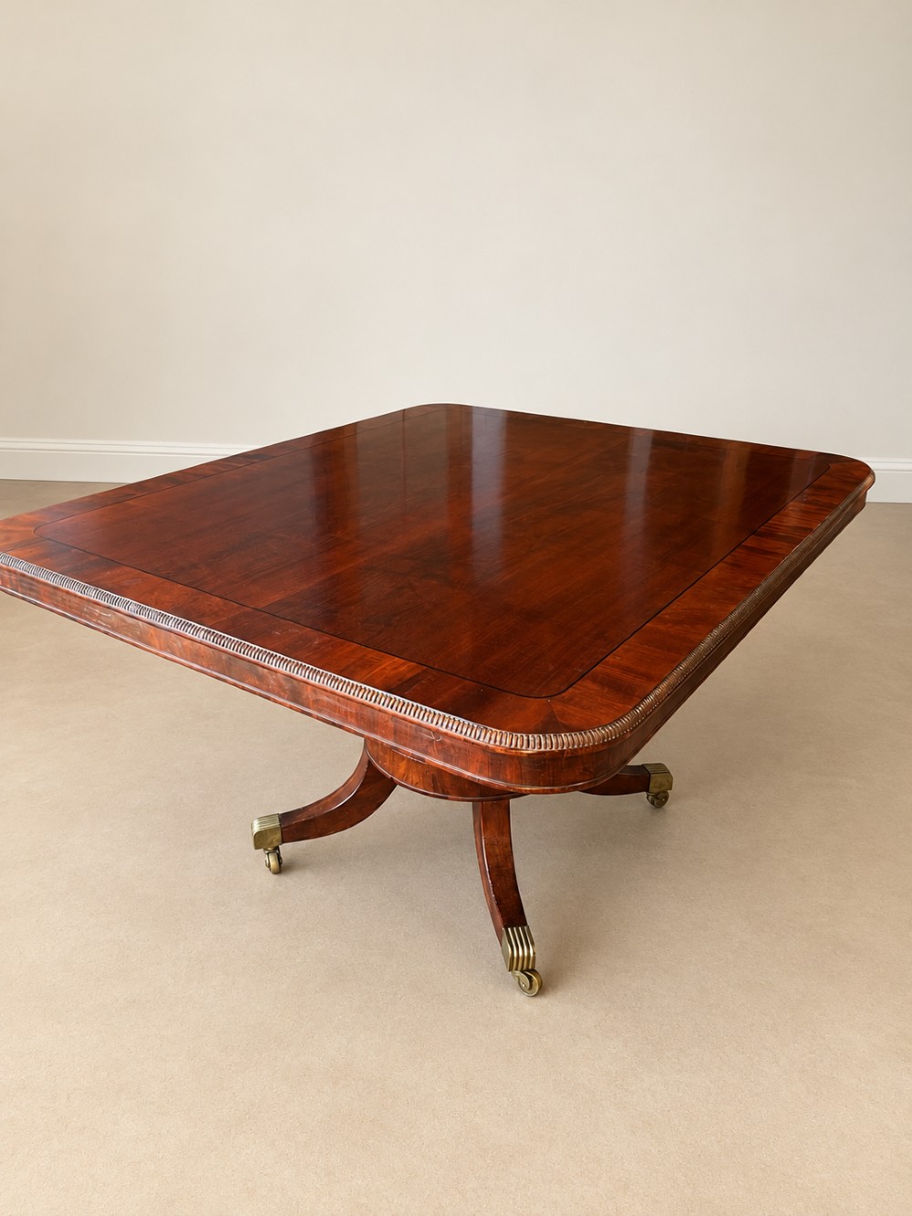 A Regency period mahogany dining table featuring a square top with rounded corners, supported by a central pedestal and four splayed legs with brass castors. View III