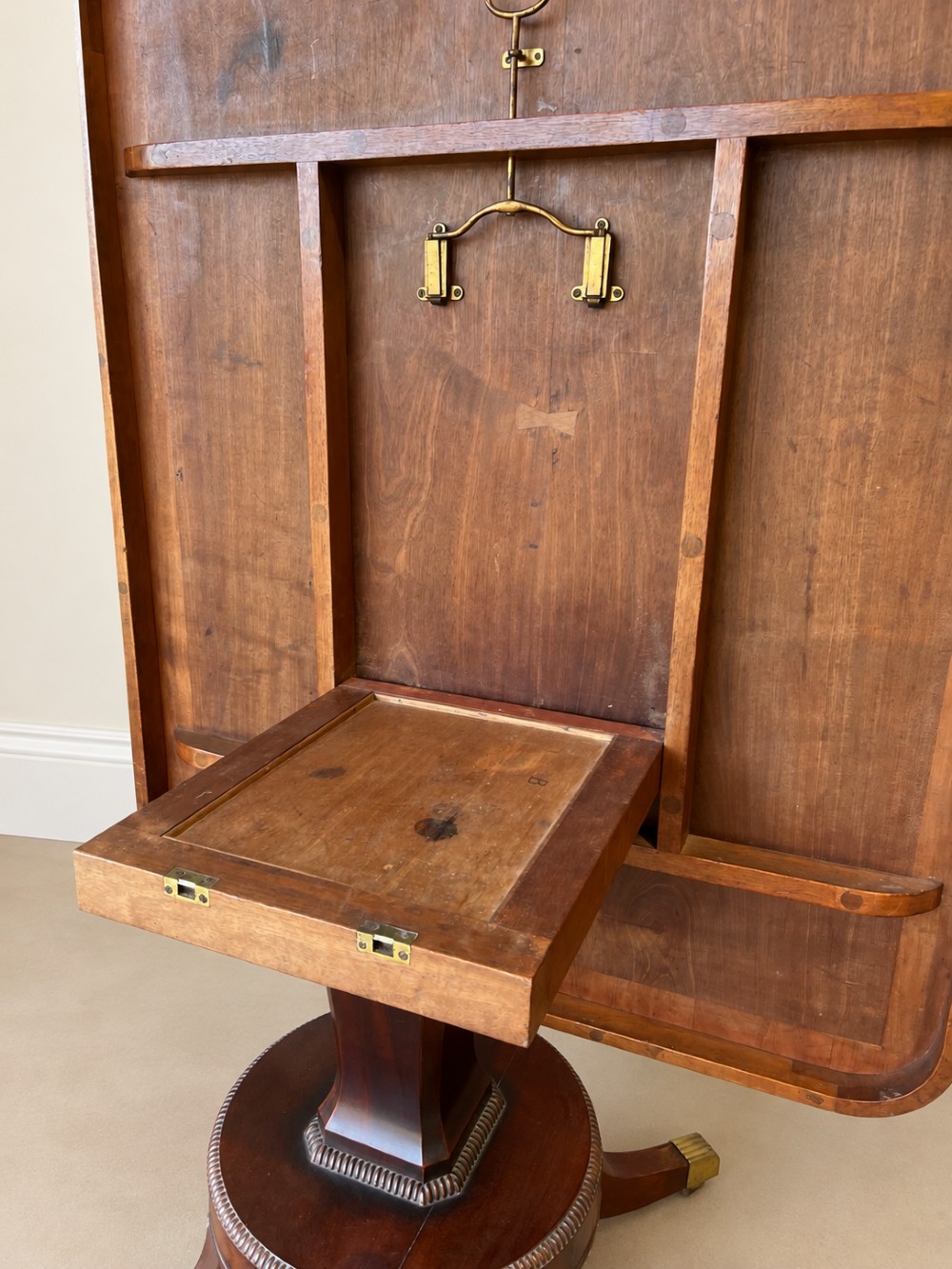 A Regency period mahogany dining table featuring a square top with rounded corners, supported by a central pedestal and four splayed legs with brass castors. View V