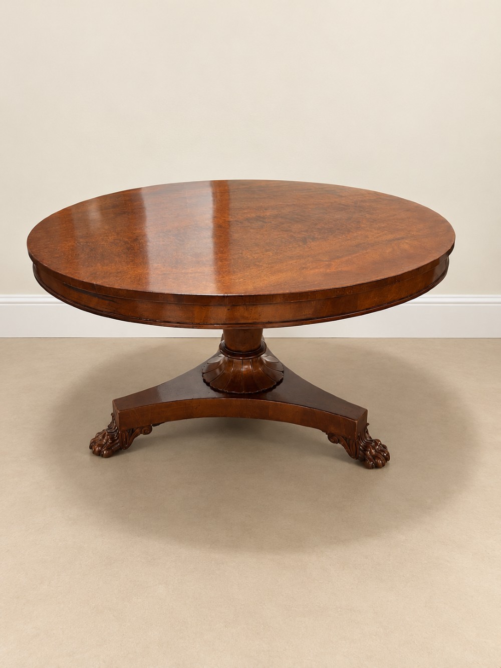 A 19th-century circular mahogany dining table featuring a polished top, turned central column with gadrooned base, and a tri-form platform resting on carved claw feet.
