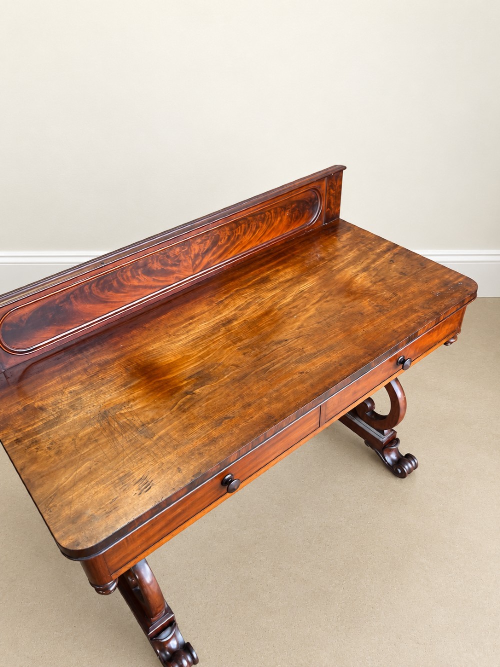A 19th-century mahogany writing desk with a low gallery back, two frieze drawers, carved scroll trestle legs, and a turned stretcher. View II