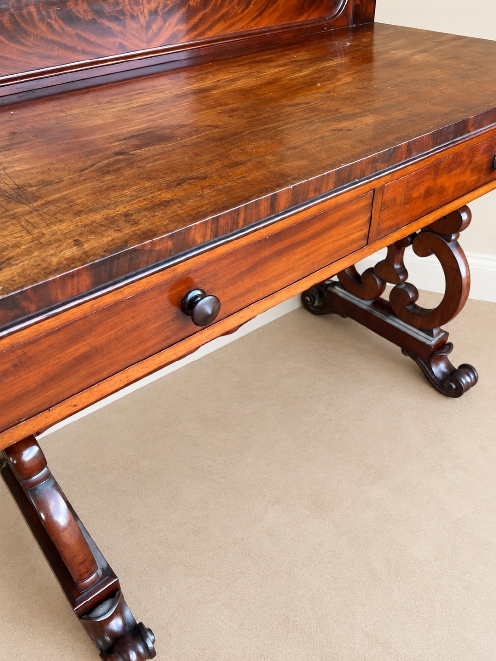 A 19th-century mahogany writing desk with a low gallery back, two frieze drawers, carved scroll trestle legs, and a turned stretcher. View VI