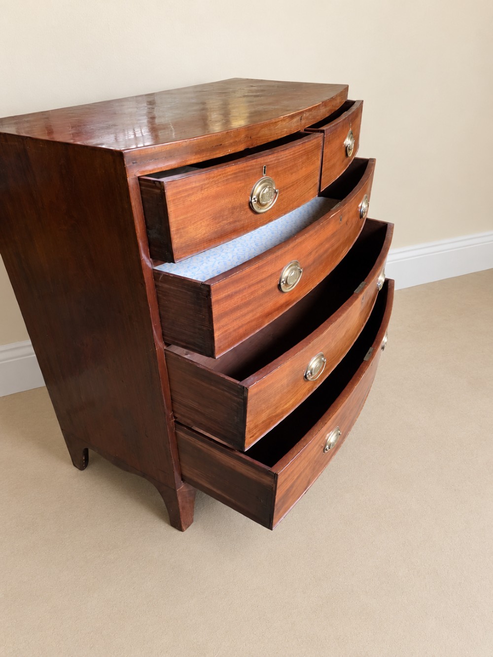 A nineteenth-century mahogany bowfront chest of drawers featuring two short drawers above three long graduated drawers with oval brass handles and splayed bracket feet. View VI