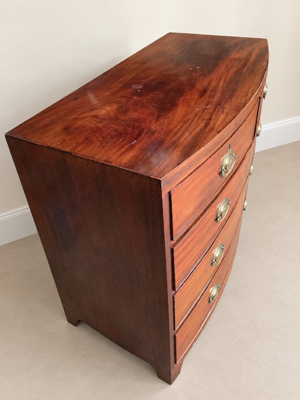 A nineteenth-century mahogany bowfront chest of drawers featuring two short drawers above three long graduated drawers with oval brass handles and splayed bracket feet. View VII