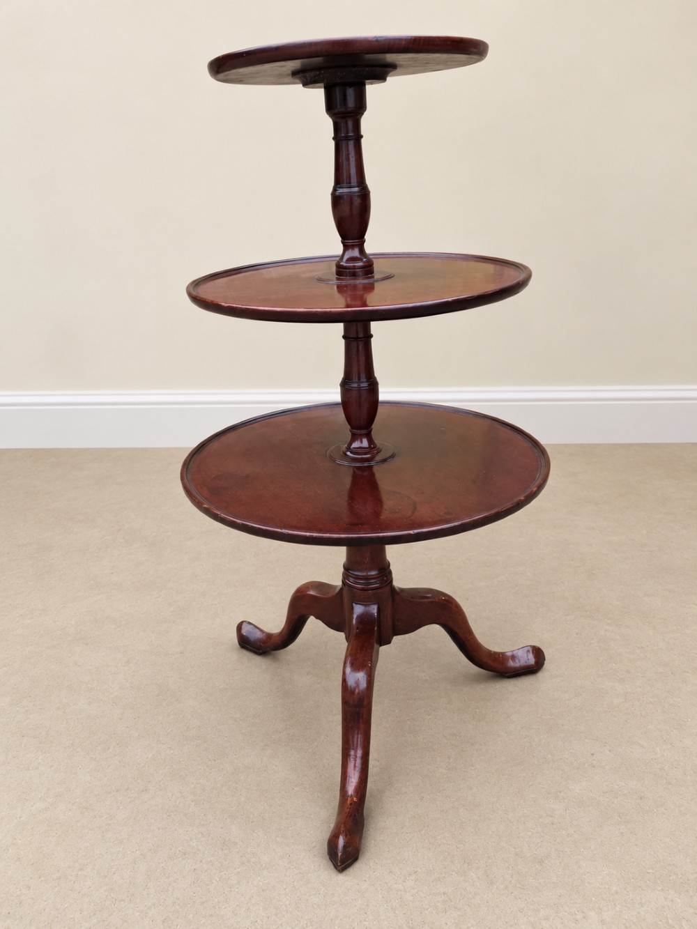A Georgian mahogany three-tiered dumb waiter with graduated circular trays supported by a turned central pillar on a tripod base.