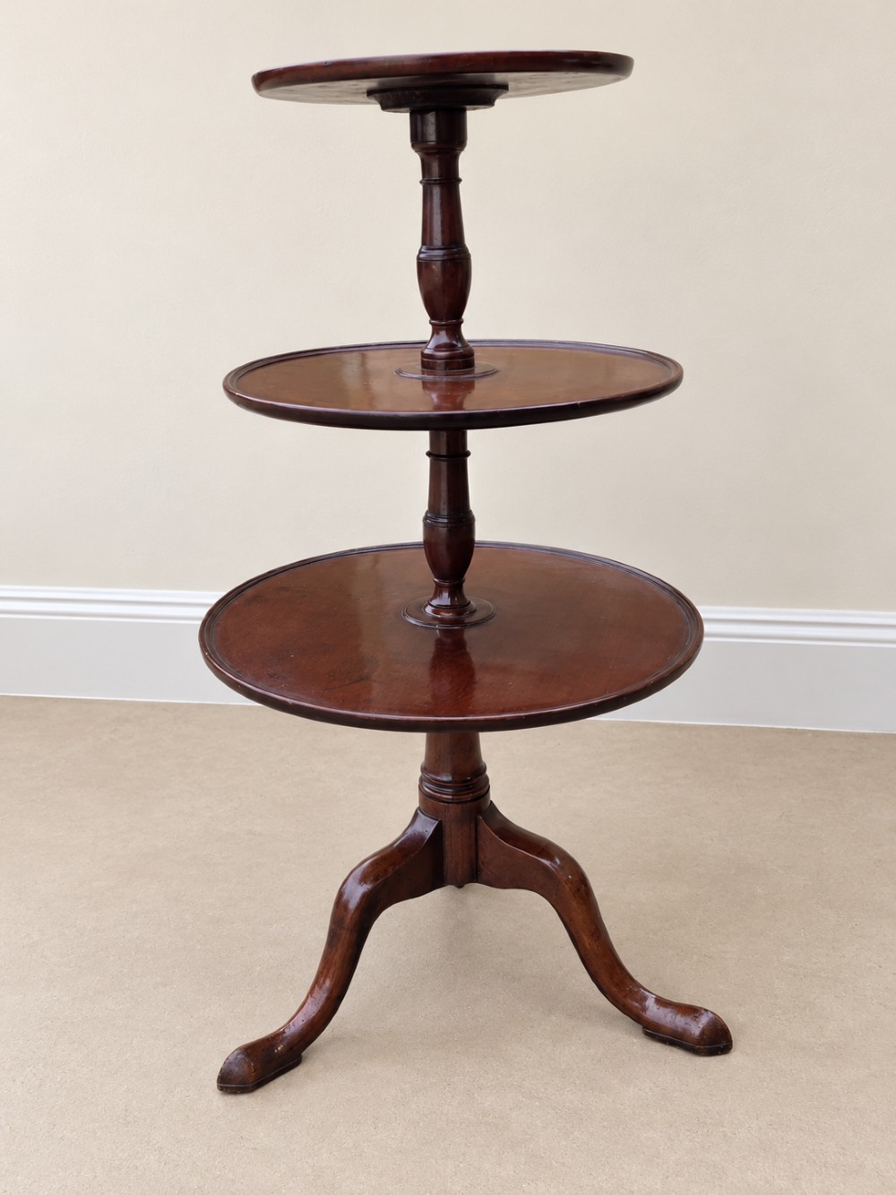 A Georgian mahogany three-tiered dumb waiter with graduated circular trays supported by a turned central pillar on a tripod base. View VIII