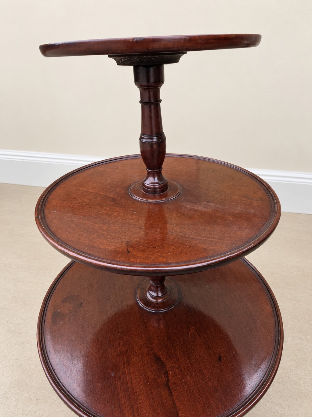 A Georgian mahogany three-tiered dumb waiter with graduated circular trays supported by a turned central pillar on a tripod base. View IX
