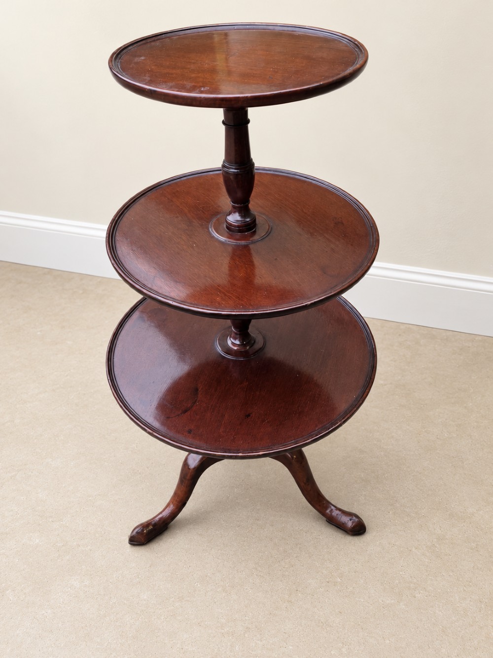 A Georgian mahogany three-tiered dumb waiter with graduated circular trays supported by a turned central pillar on a tripod base. View X