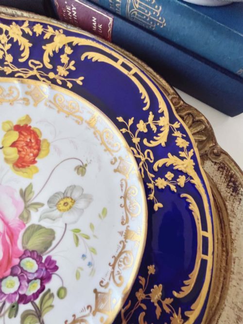 fig 1. An antique Coalport porcelain dessert plate featuring a central hand-painted floral bouquet surrounded by a rich cobalt blue rim decorated with ornate gold gilding.