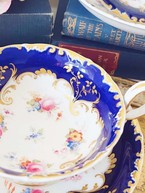 fig 1. An antique bone china teacup and saucer featuring cobalt blue borders with gold scrollwork and hand-painted floral centres.