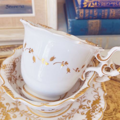 fig 1. A Regency era porcelain tea trio comprising a teacup, coffee cup, and saucer decorated with blue floral hand-painting and gold leaf gilding.