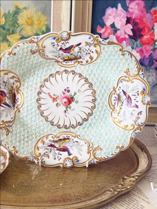 fig 1. An oval antique porcelain serving dish featuring hand-painted birds in cartouches, a central pink rose, a turquoise pattern ground, and a scalloped gilded rim.