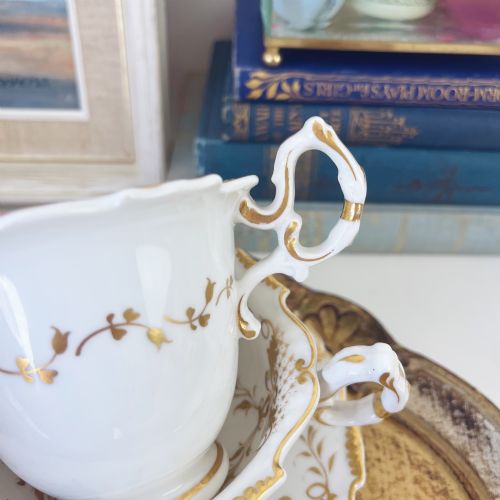 fig 1. An early nineteenth-century porcelain tea and coffee cup trio featuring hand-painted blue floral motifs and gilt scroll detailing on white ground.
