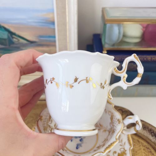 fig 2. An early nineteenth-century porcelain tea and coffee cup trio featuring hand-painted blue floral motifs and gilt scroll detailing on white ground.