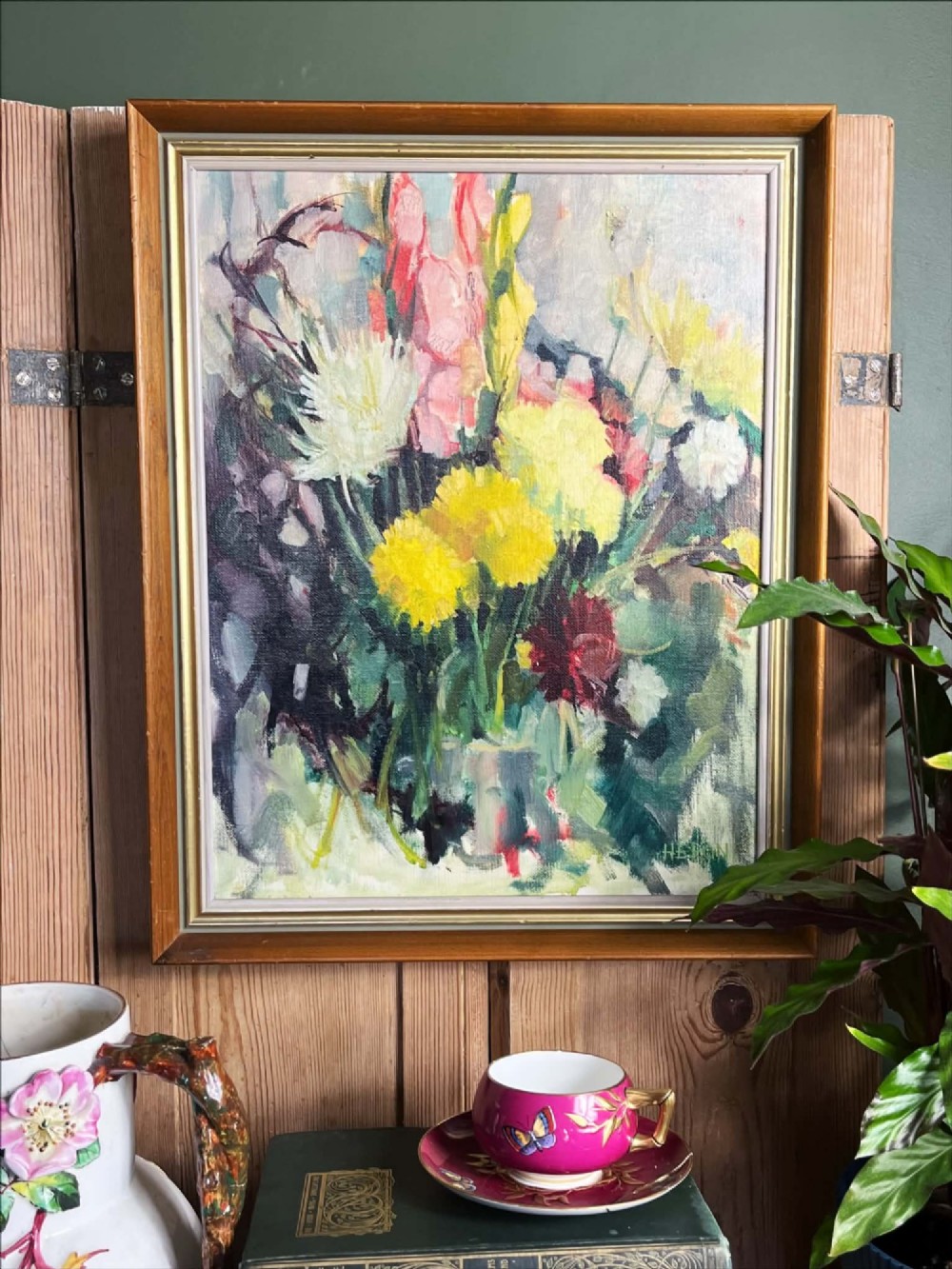 A framed mid-century oil on board painting featuring a colourful floral still life composition with yellow, pink, and green tones set within a wooden frame.