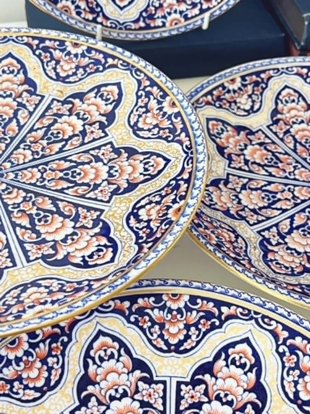 A seven-piece porcelain dessert service featuring intricate cobalt blue, terracotta, and gold geometric star patterns, comprising six plates and a comport. View V