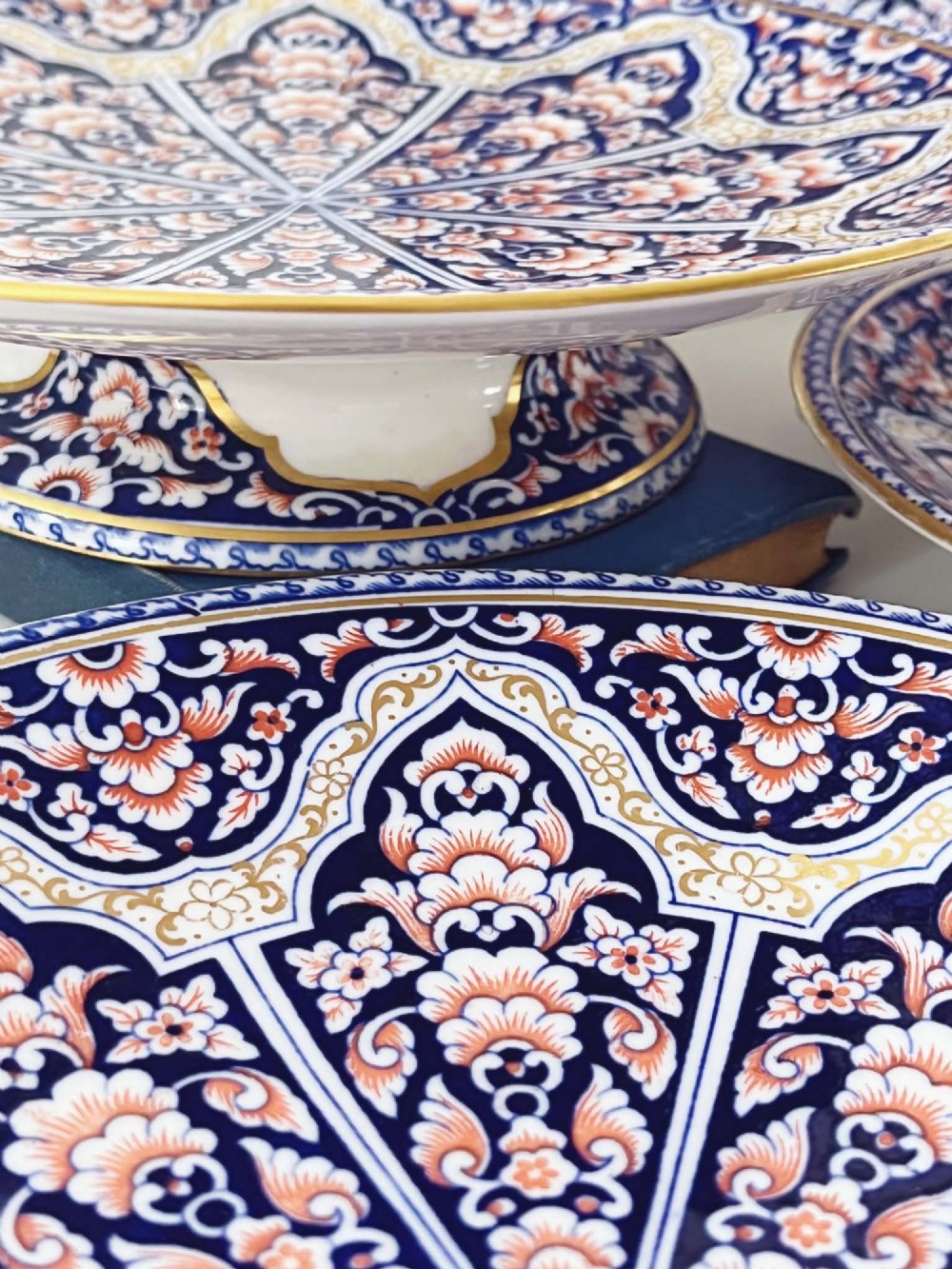 A seven-piece porcelain dessert service featuring intricate cobalt blue, terracotta, and gold geometric star patterns, comprising six plates and a comport. View II