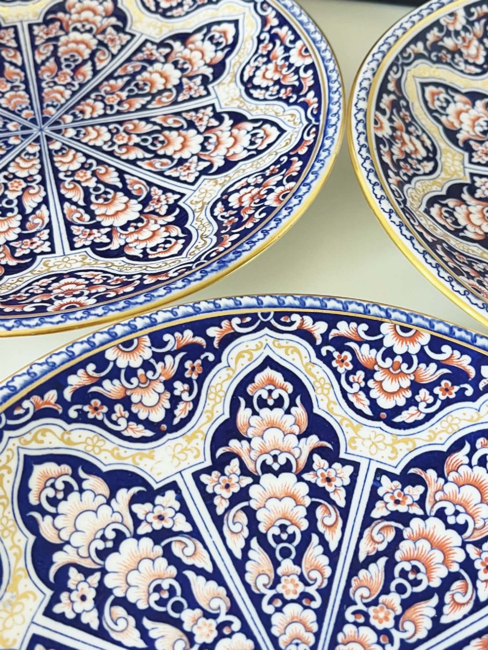 A seven-piece porcelain dessert service featuring intricate cobalt blue, terracotta, and gold geometric star patterns, comprising six plates and a comport. View IX