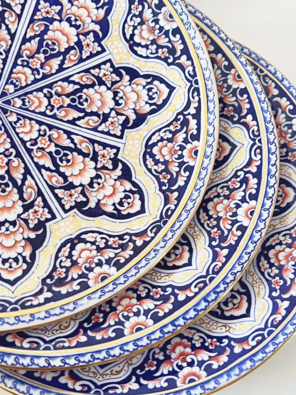 A seven-piece porcelain dessert service featuring intricate cobalt blue, terracotta, and gold geometric star patterns, comprising six plates and a comport. View X