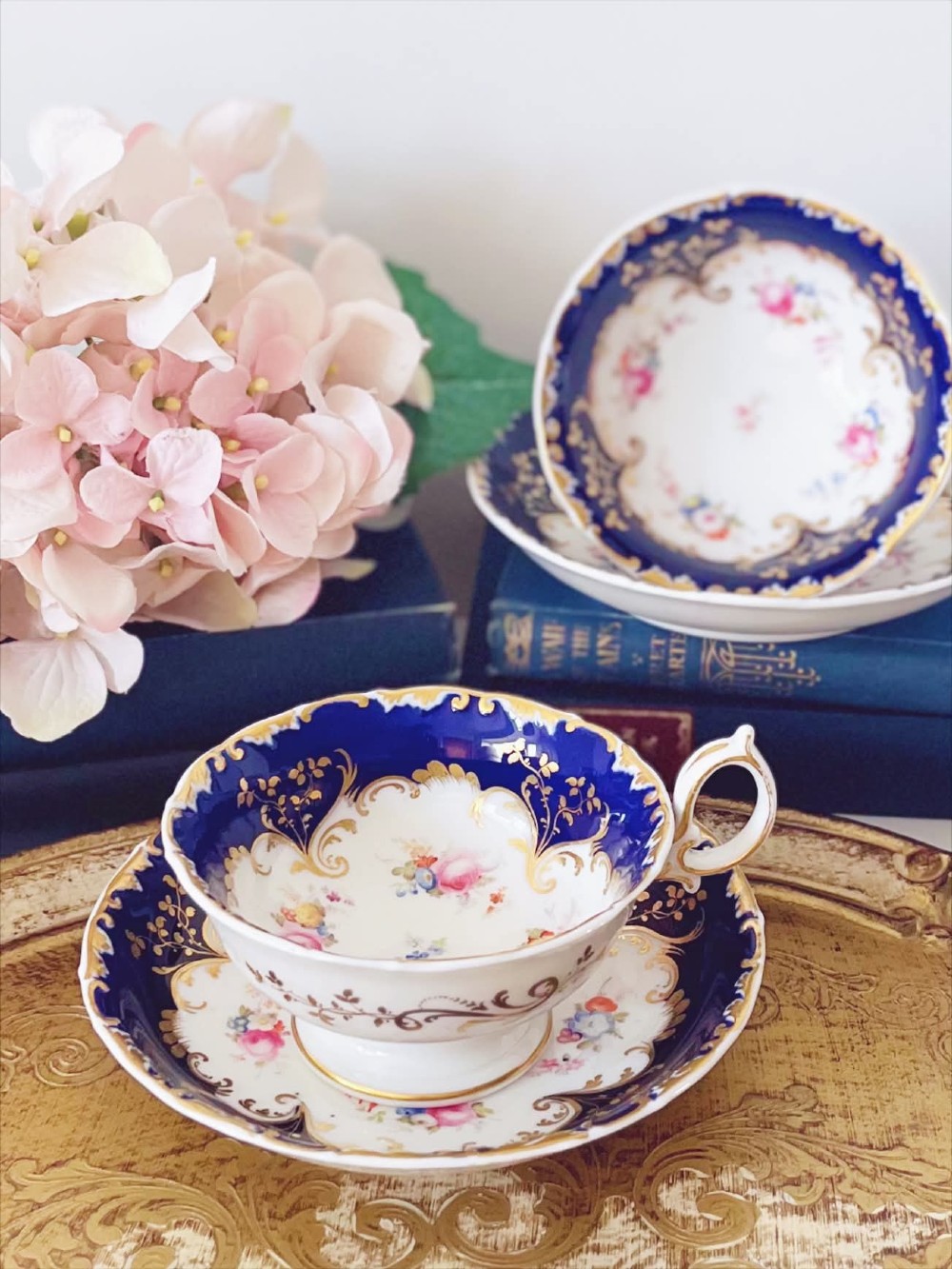 An antique bone china teacup and saucer featuring cobalt blue borders with gold scrollwork and hand-painted floral centres.