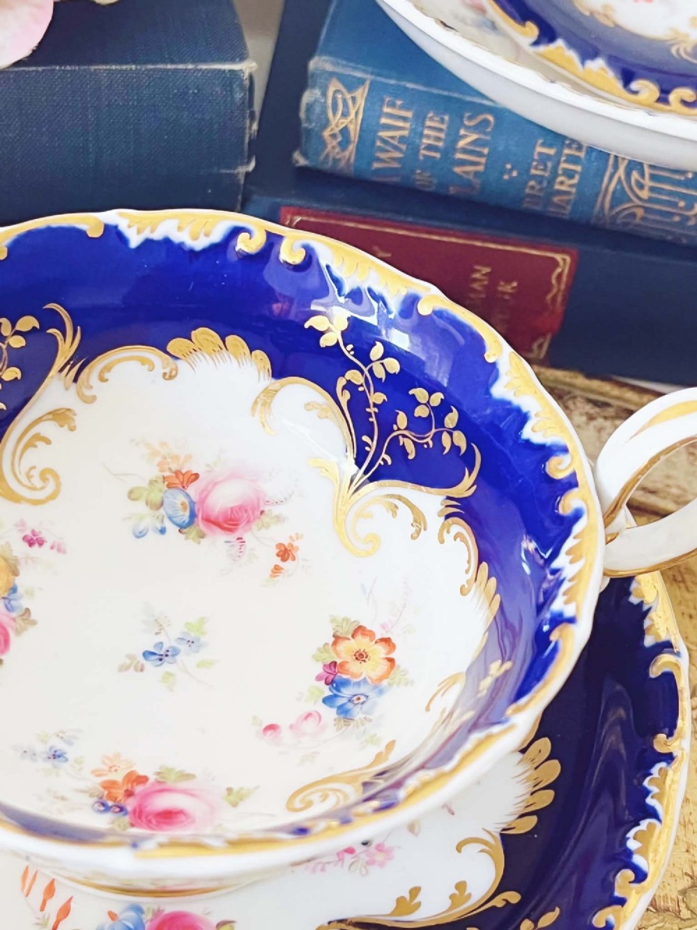 An antique bone china teacup and saucer featuring cobalt blue borders with gold scrollwork and hand-painted floral centres. View II