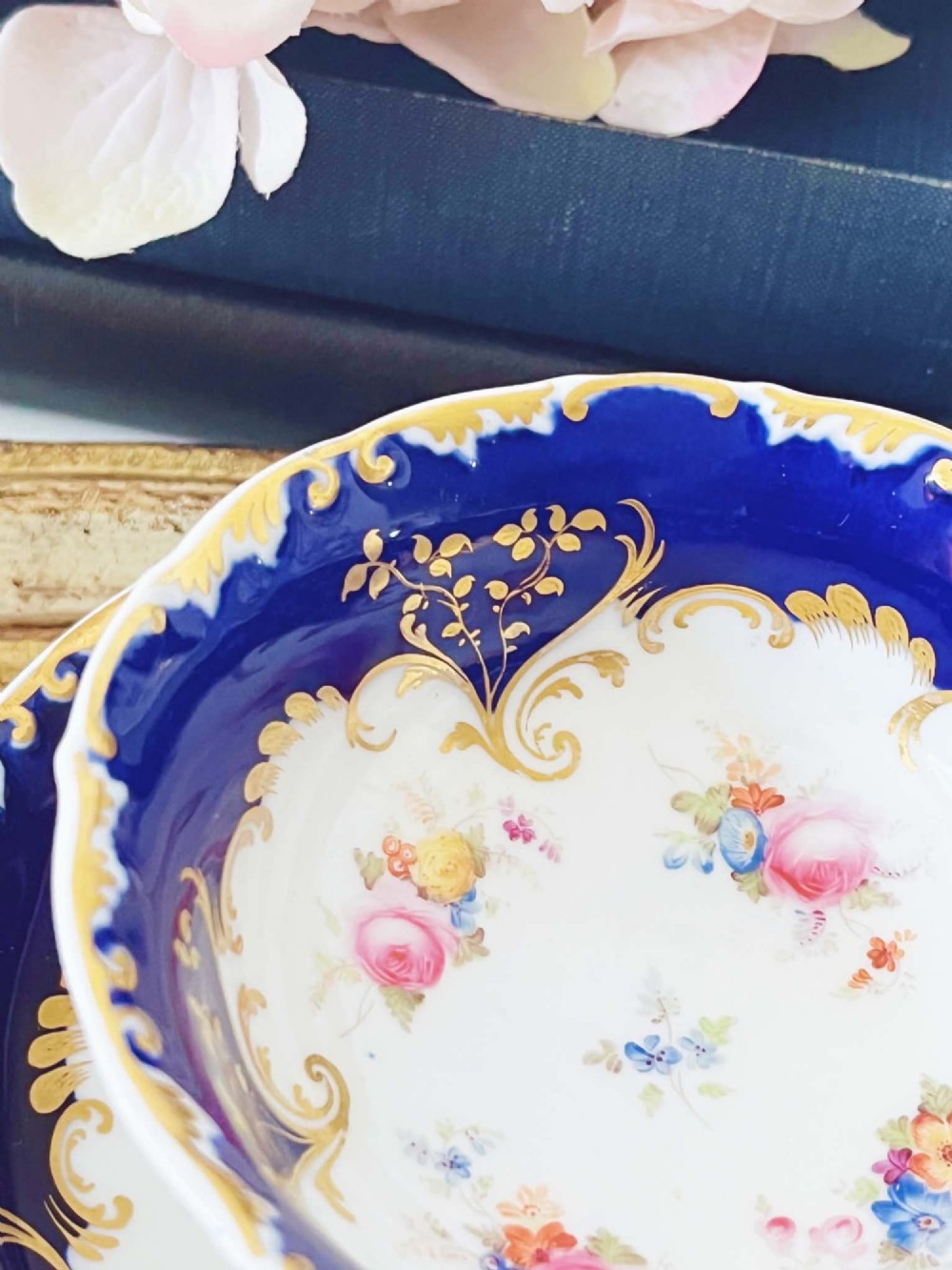 An antique bone china teacup and saucer featuring cobalt blue borders with gold scrollwork and hand-painted floral centres. View III