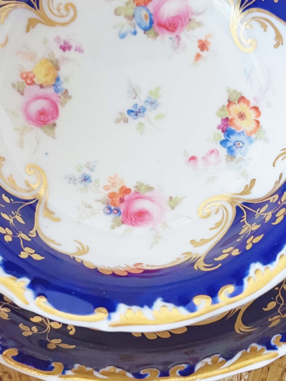 An antique bone china teacup and saucer featuring cobalt blue borders with gold scrollwork and hand-painted floral centres. View IV