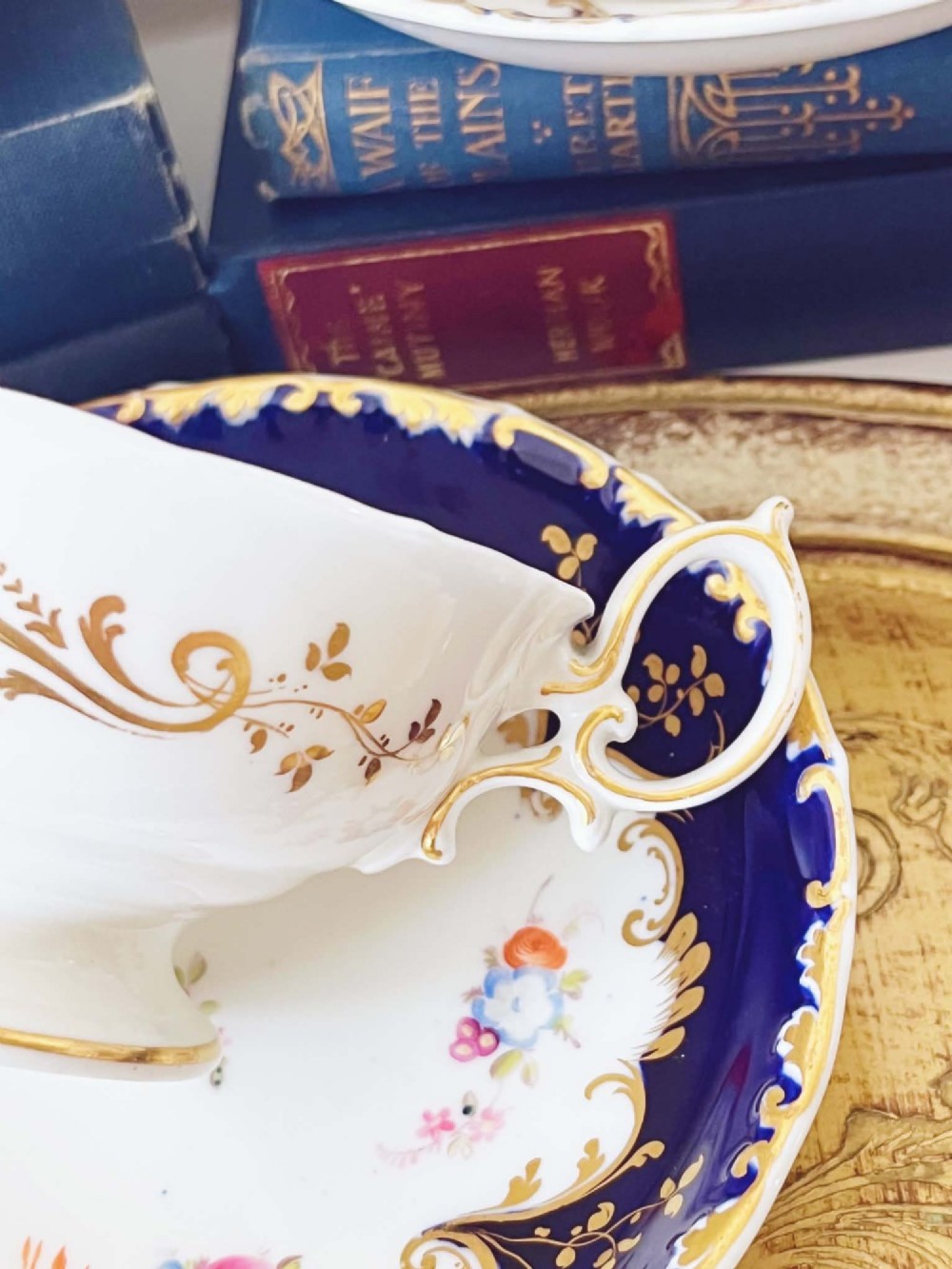 An antique bone china teacup and saucer featuring cobalt blue borders with gold scrollwork and hand-painted floral centres. View V
