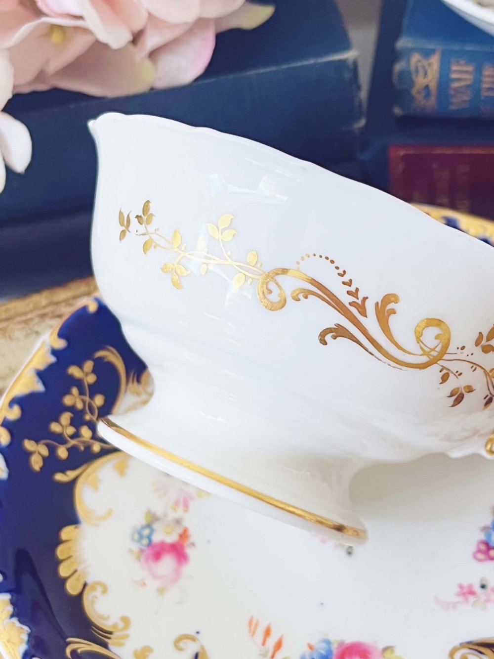 An antique bone china teacup and saucer featuring cobalt blue borders with gold scrollwork and hand-painted floral centres. View VI