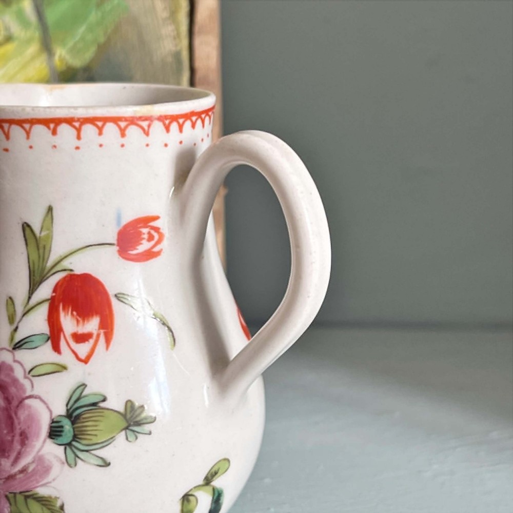 An eighteenth-century Bow soft-paste porcelain sparrowbeak cream jug hand-painted with polychrome floral sprigs and a red painted border. View II