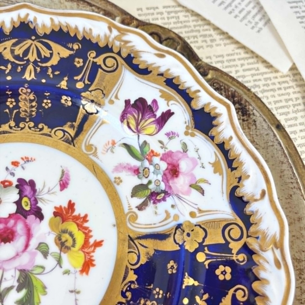 An early nineteenth-century Samuel Alcock porcelain dessert plate featuring a cobalt blue ground, intricate gilt scrolling, and hand-painted floral cartouches. View II