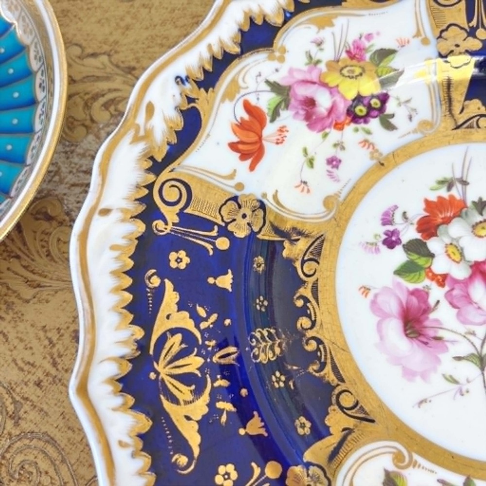 An early nineteenth-century Samuel Alcock porcelain dessert plate featuring a cobalt blue ground, intricate gilt scrolling, and hand-painted floral cartouches. View V