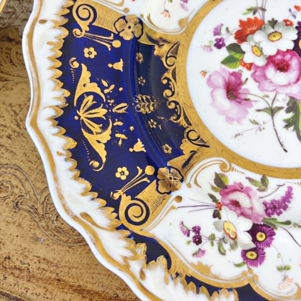 An early nineteenth-century Samuel Alcock porcelain dessert plate featuring a cobalt blue ground, intricate gilt scrolling, and hand-painted floral cartouches. View VI