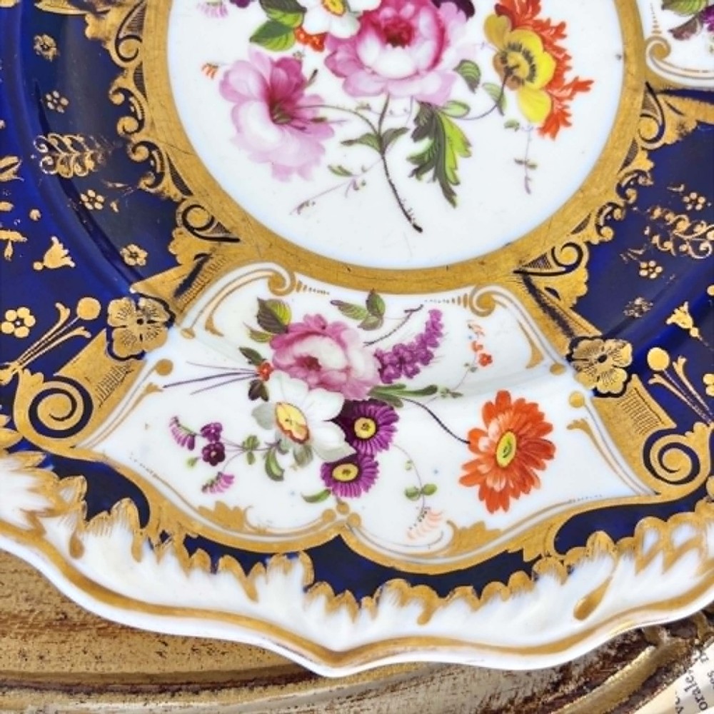 An early nineteenth-century Samuel Alcock porcelain dessert plate featuring a cobalt blue ground, intricate gilt scrolling, and hand-painted floral cartouches. View VII