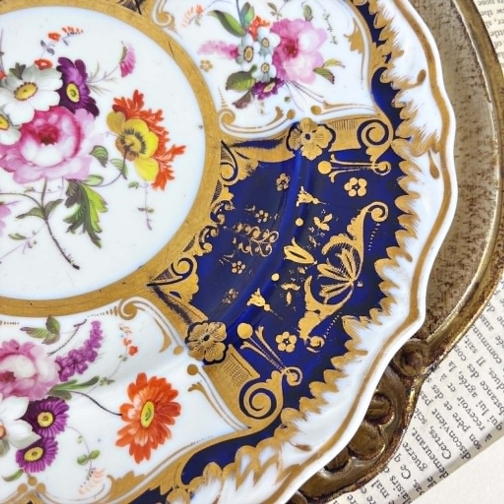 An early nineteenth-century Samuel Alcock porcelain dessert plate featuring a cobalt blue ground, intricate gilt scrolling, and hand-painted floral cartouches. View VIII