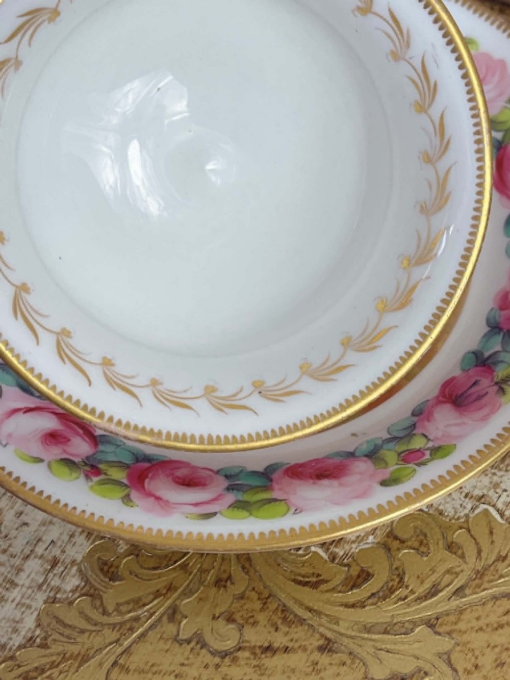 An antique porcelain teacup and matching saucer featuring hand-painted pink cabbage roses, green leaves, and gold scroll decorations. View II
