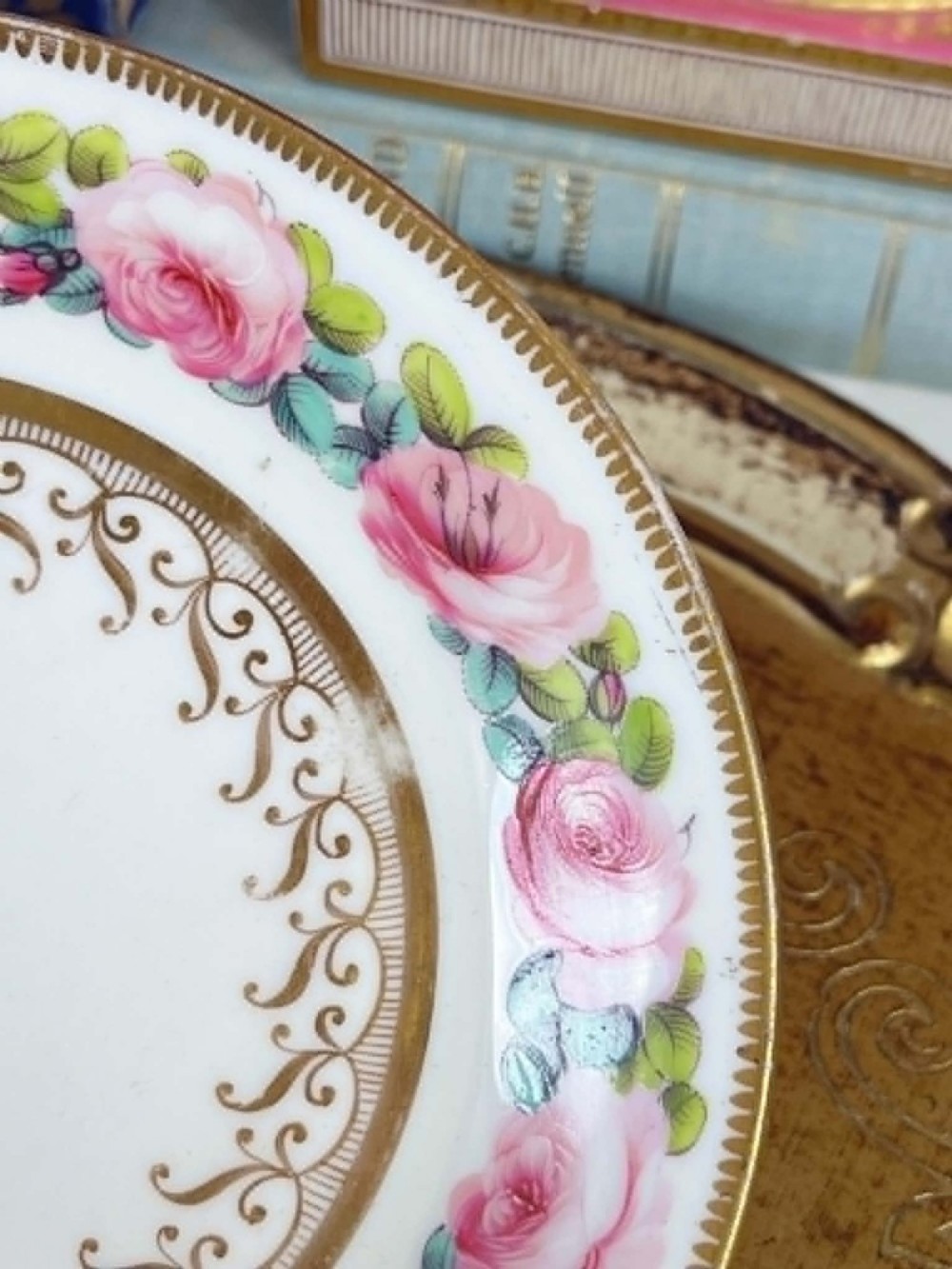 An antique porcelain teacup and matching saucer featuring hand-painted pink cabbage roses, green leaves, and gold scroll decorations. View V