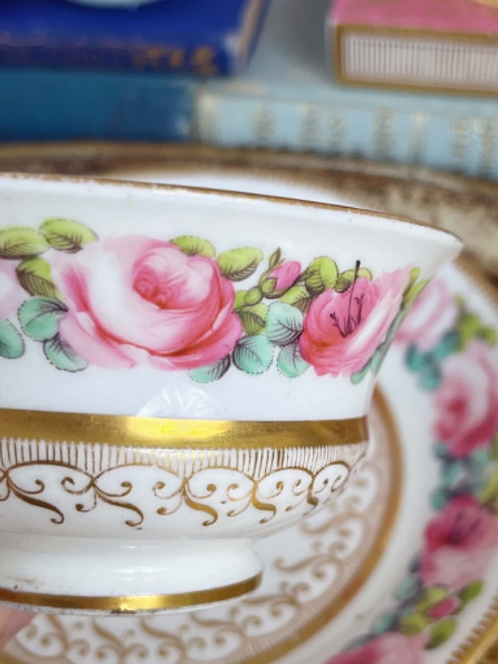 An antique porcelain teacup and matching saucer featuring hand-painted pink cabbage roses, green leaves, and gold scroll decorations. View IX