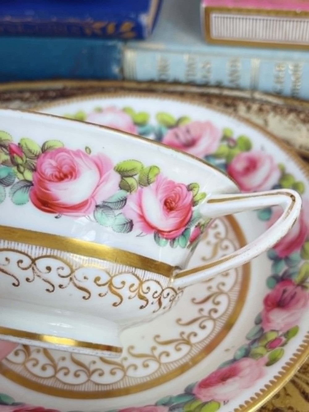An antique porcelain teacup and matching saucer featuring hand-painted pink cabbage roses, green leaves, and gold scroll decorations. View XII