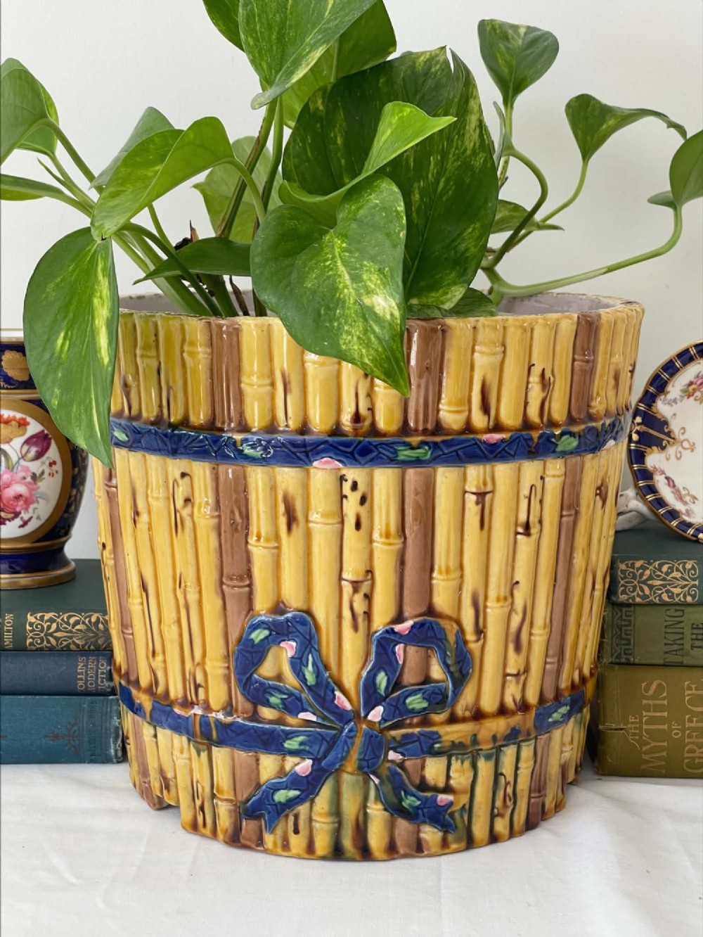 A cylindrical Victorian majolica jardiniere decorated with a moulded bamboo cane pattern in yellow and brown tones, wrapped with a blue ribbon tied in a bow.