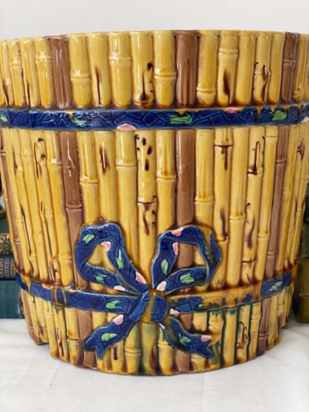 A cylindrical Victorian majolica jardiniere decorated with a moulded bamboo cane pattern in yellow and brown tones, wrapped with a blue ribbon tied in a bow. View II