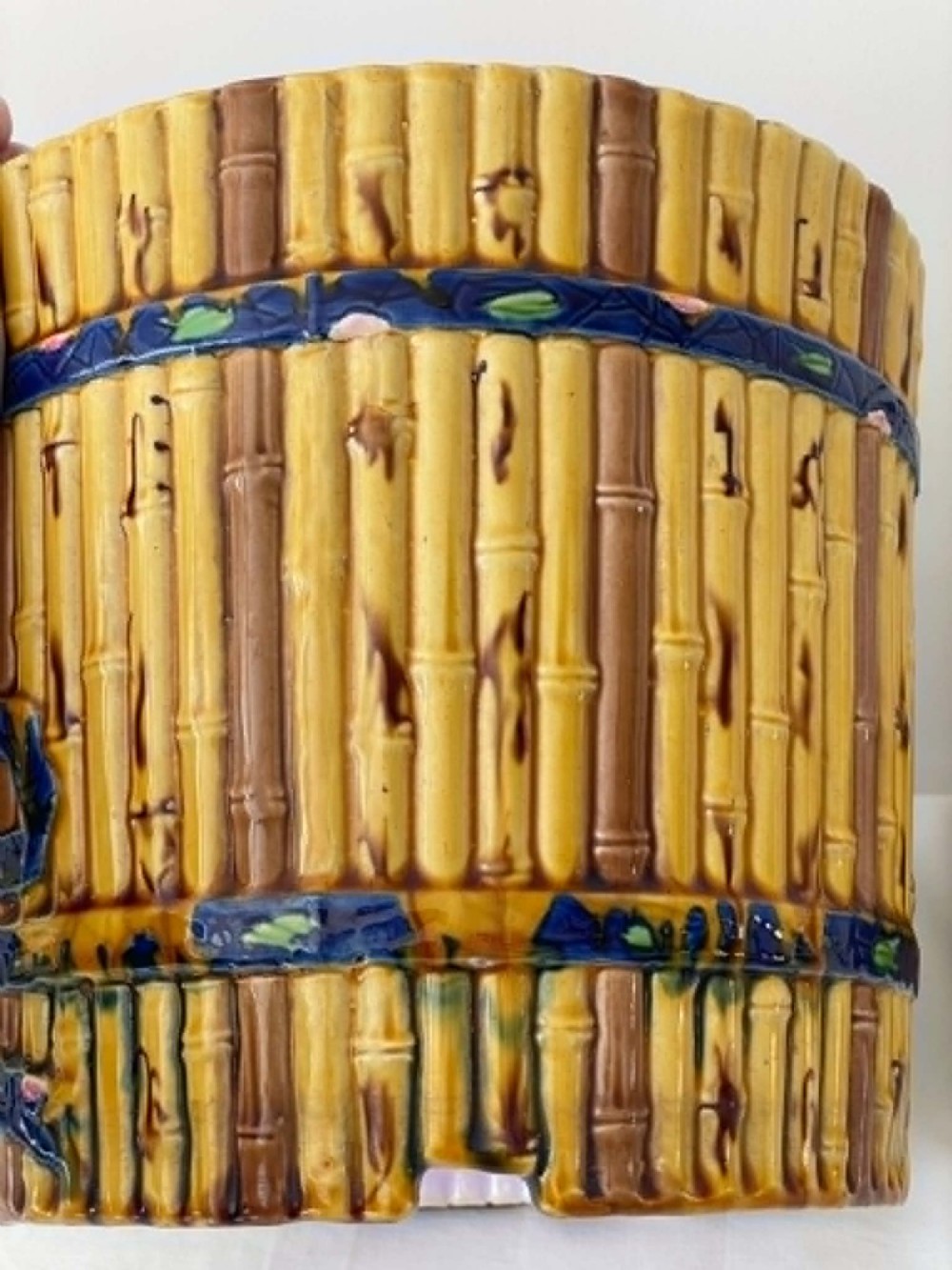 A cylindrical Victorian majolica jardiniere decorated with a moulded bamboo cane pattern in yellow and brown tones, wrapped with a blue ribbon tied in a bow. View III