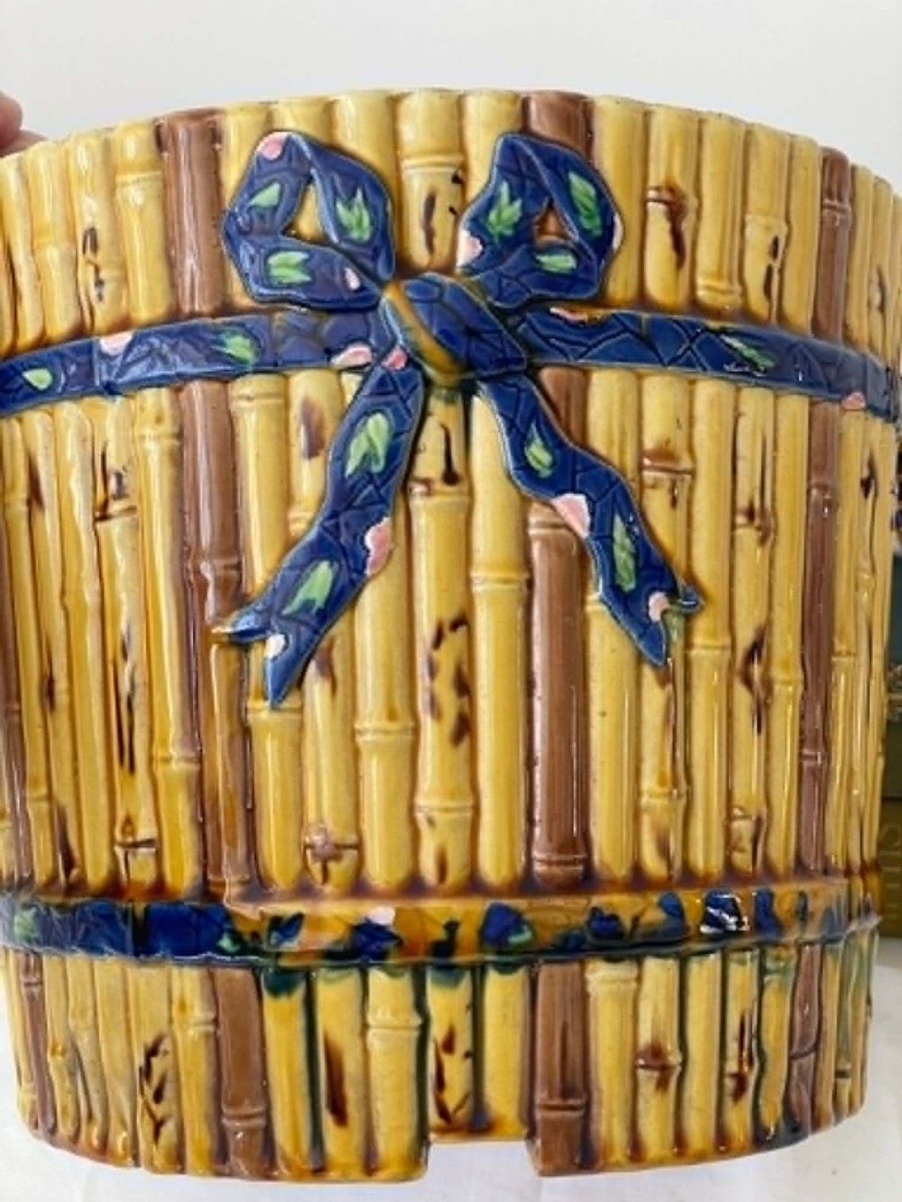 A cylindrical Victorian majolica jardiniere decorated with a moulded bamboo cane pattern in yellow and brown tones, wrapped with a blue ribbon tied in a bow. View VI