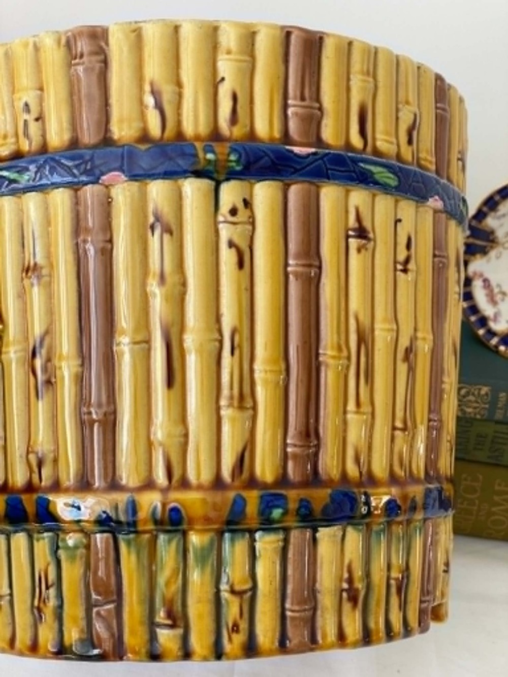 A cylindrical Victorian majolica jardiniere decorated with a moulded bamboo cane pattern in yellow and brown tones, wrapped with a blue ribbon tied in a bow. View VII